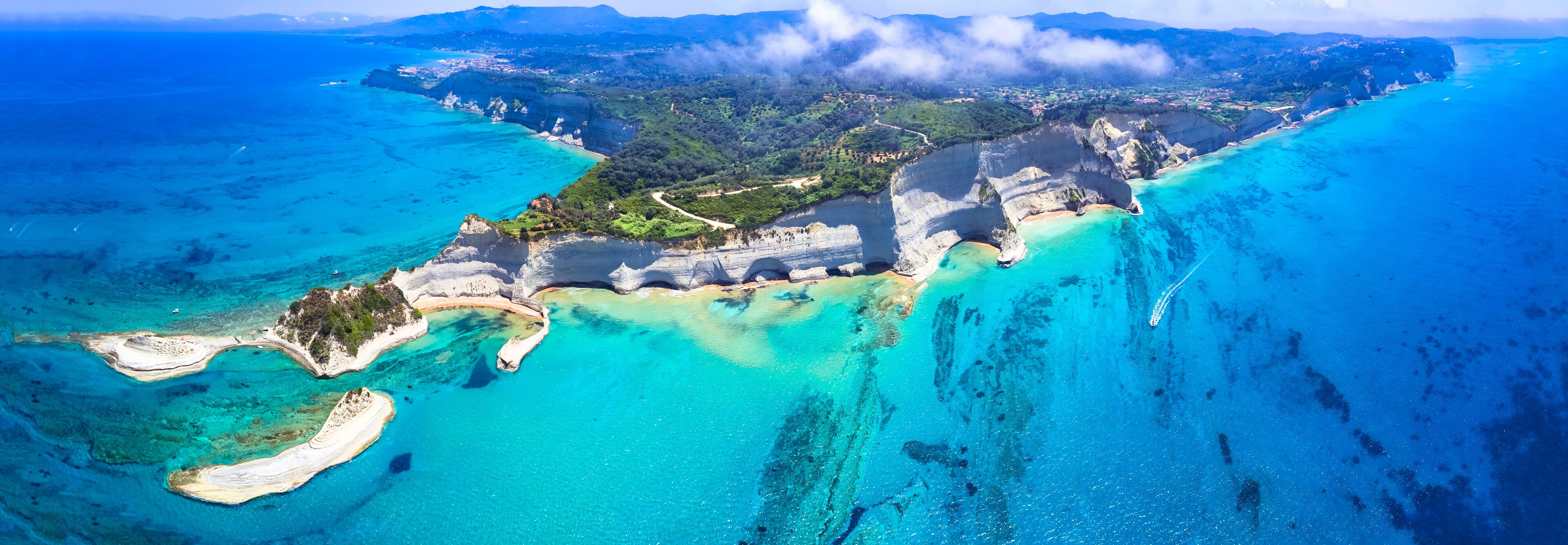 Vista aérea de un paisaje costero con aguas turquesas cristalinas, playas de arena blanca y un litoral rocoso con acantilados.