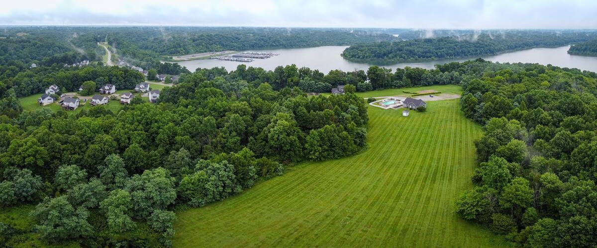 A lush green landscape with a large lake, surrounded by dense forests and residential houses.