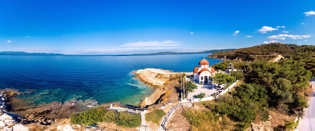 A coastal town with a prominent church, clear blue sea, and a hilly backdrop.