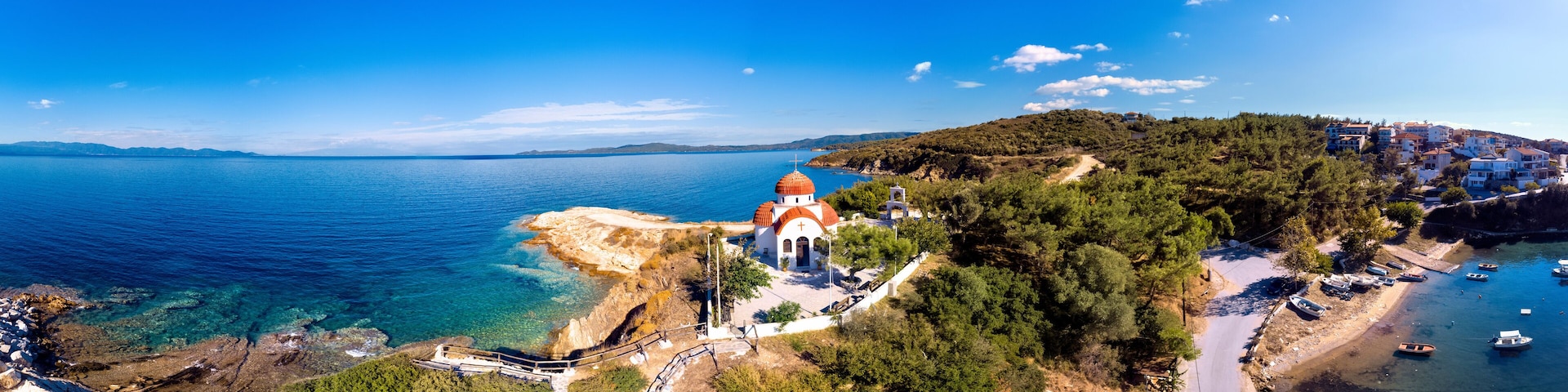 A coastal town with a prominent church, clear blue sea, and a hilly backdrop.