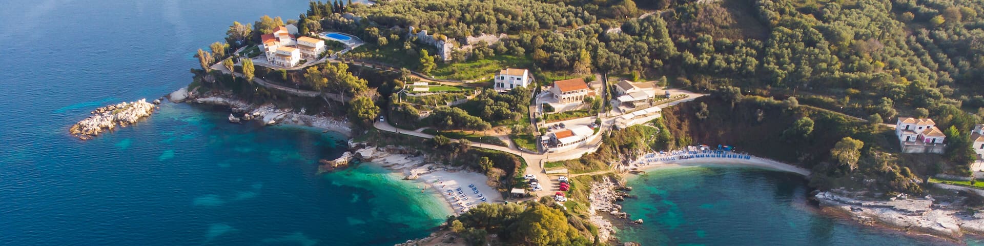 An aerial view of a coastal area with clear turquoise waters, rocky outcrops, and scattered buildings.