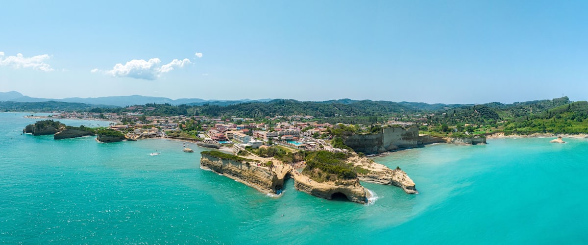 A coastal town with a prominent rocky peninsula, clear turquoise waters, and a backdrop of green hills.