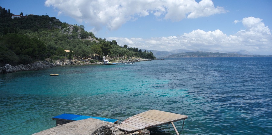 View of the sea and mountains at the village of Nissaki on the beautiful Greek island of Corfu. A small wooden jetty in the foreground and pine clad cliffs in the middle distance. Copy space.