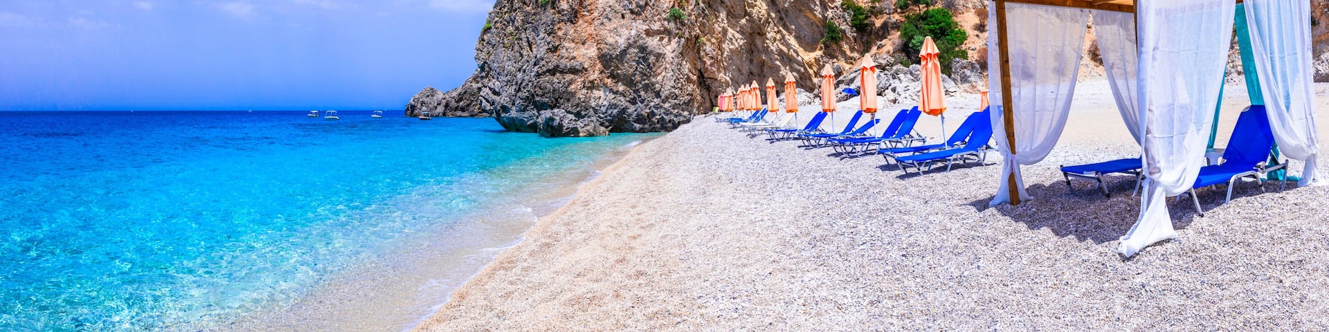 Corfu island beach view in Greece with luxury beach cabana and turquoise sea. Beautiful empty paradise coastline with white pebbles, sunbeds and cliff mountains panorama. World Print 13k