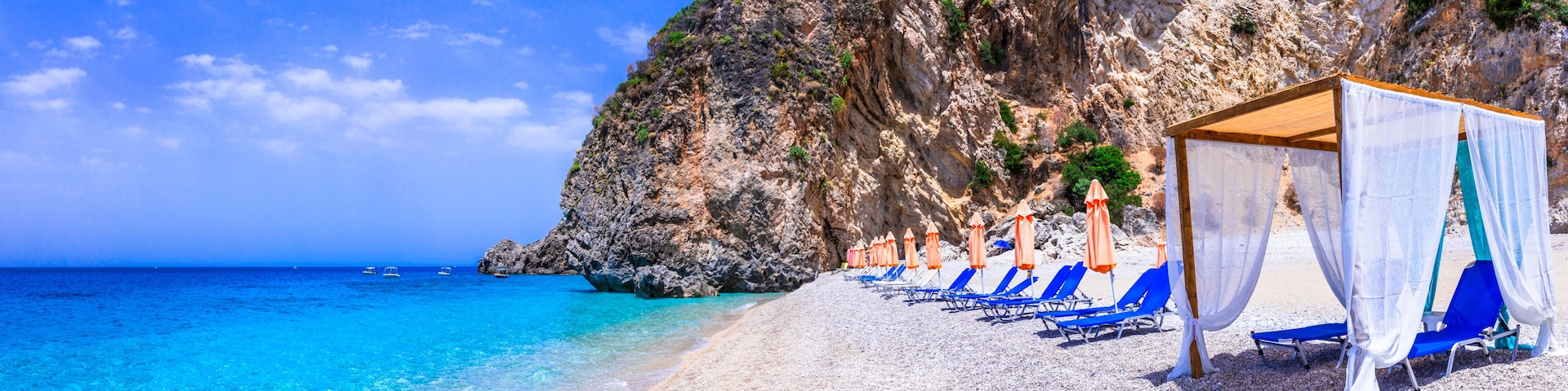 Una playa con agua turquesa cristalina, un acantilado rocoso y sillas de baño azules.