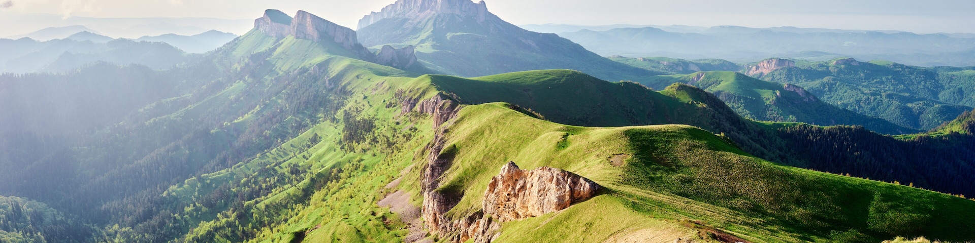 Eine gebirgige Landschaft mit grünen Hügeln und felsigen Ausläufern.