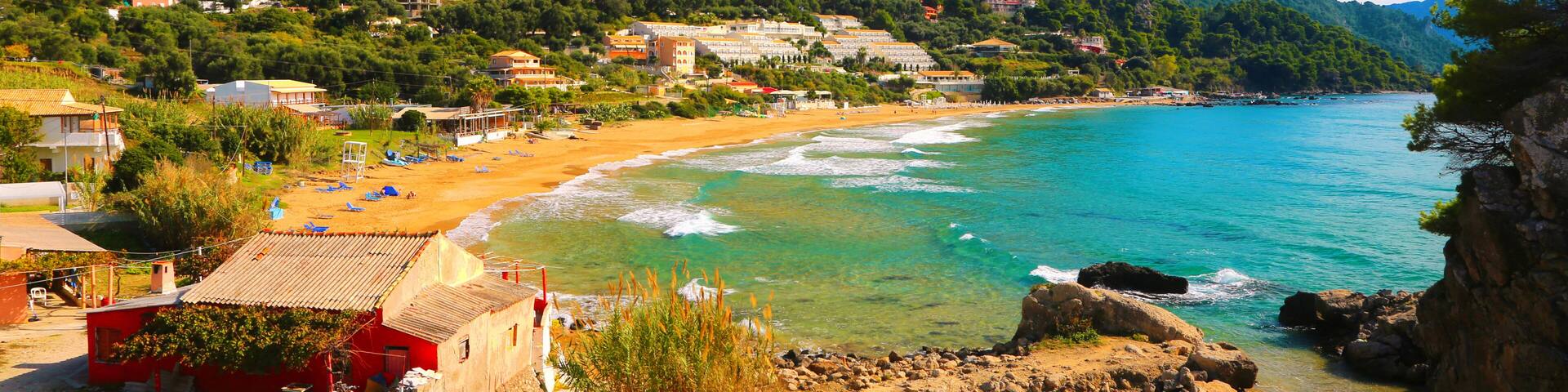 A coastal town with a sandy beach, turquoise waters, and a backdrop of green hills.