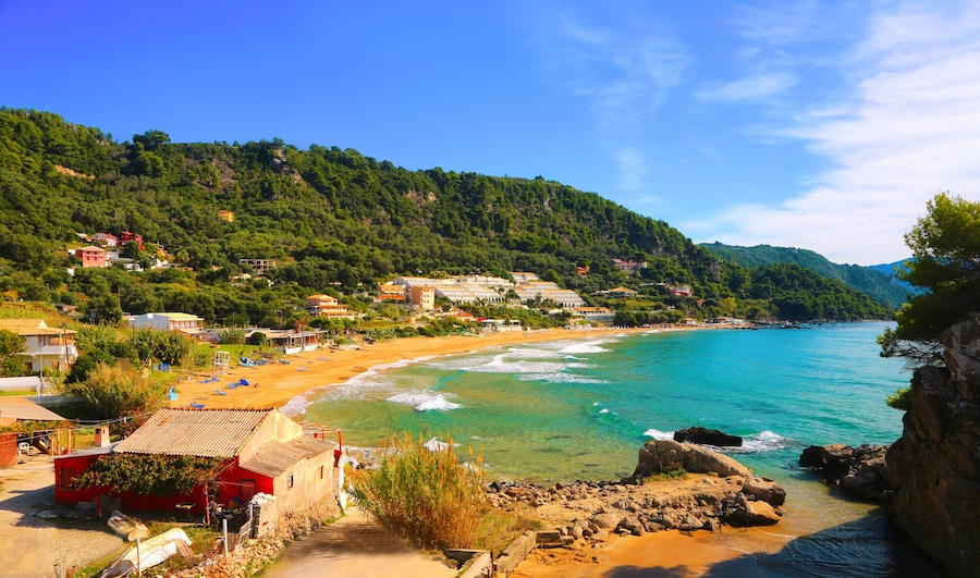 A coastal town with a sandy beach, turquoise waters, and a backdrop of green hills.