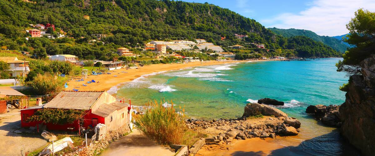 A coastal town with a sandy beach, turquoise waters, and a backdrop of green hills.