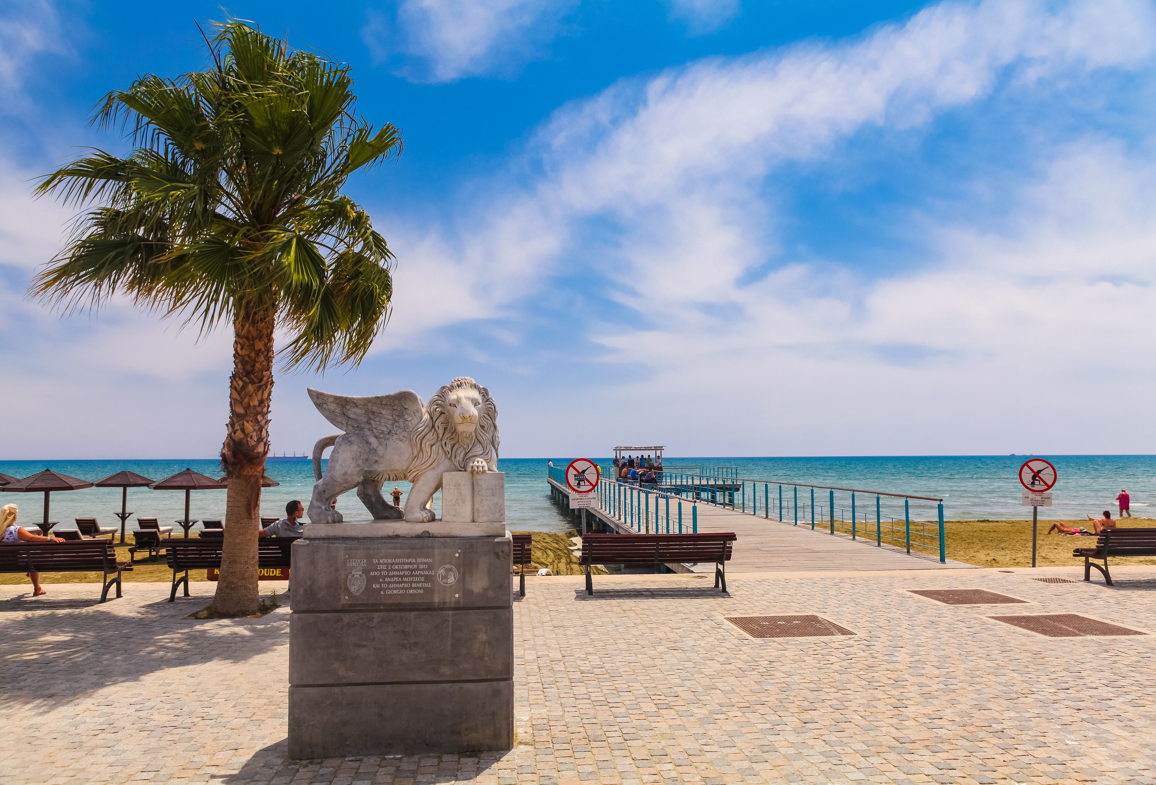 Uma praia com estátua de leão, palmeiras e céu azul límpido.