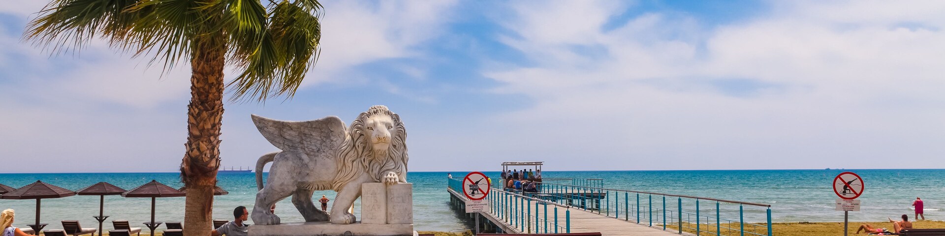 Uma praia com estátua de leão, palmeiras e céu azul límpido.