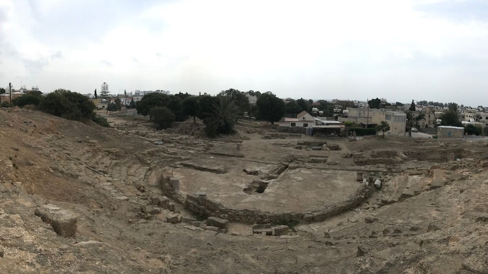An archaeological site with ancient ruins and modern buildings in the background.