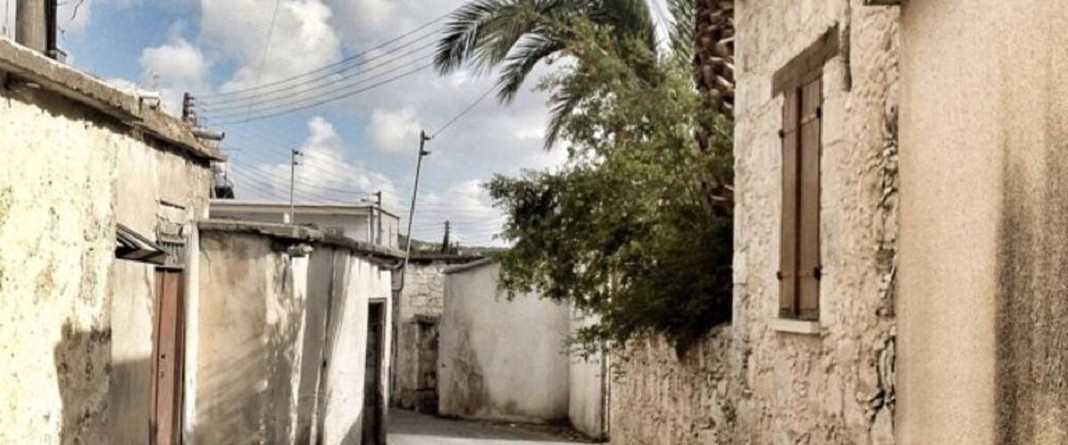 A narrow street flanked by old buildings with palm trees and power lines.