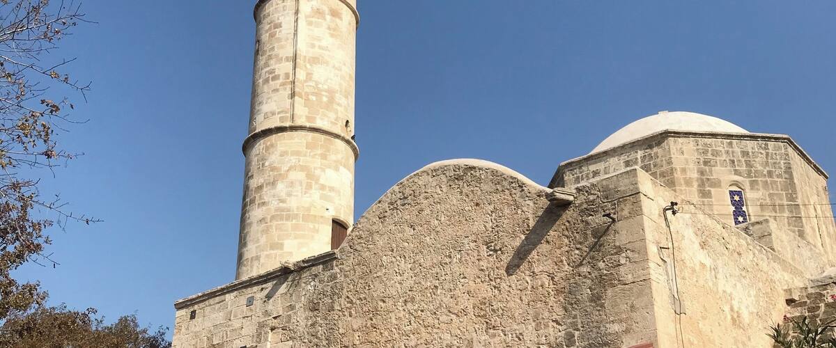 A tall stone minaret with a dome and a smaller adjacent building.