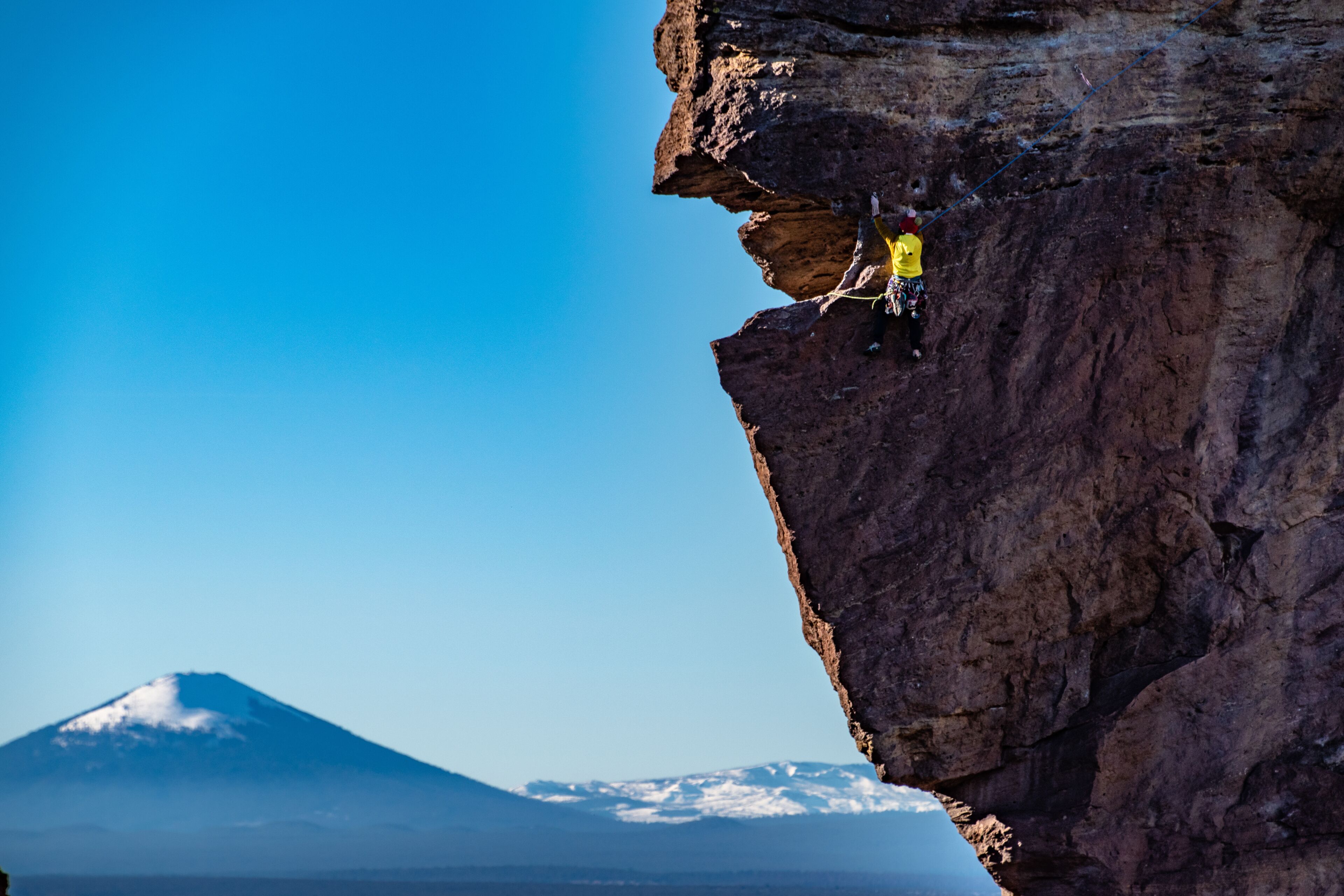 Una persona escalando una pared rocosa empinada con una montaña al fondo.