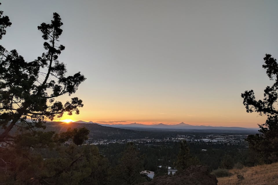 Un coucher de soleil sur un paysage montagneux, avec une ville située dans la vallée en contrebas.