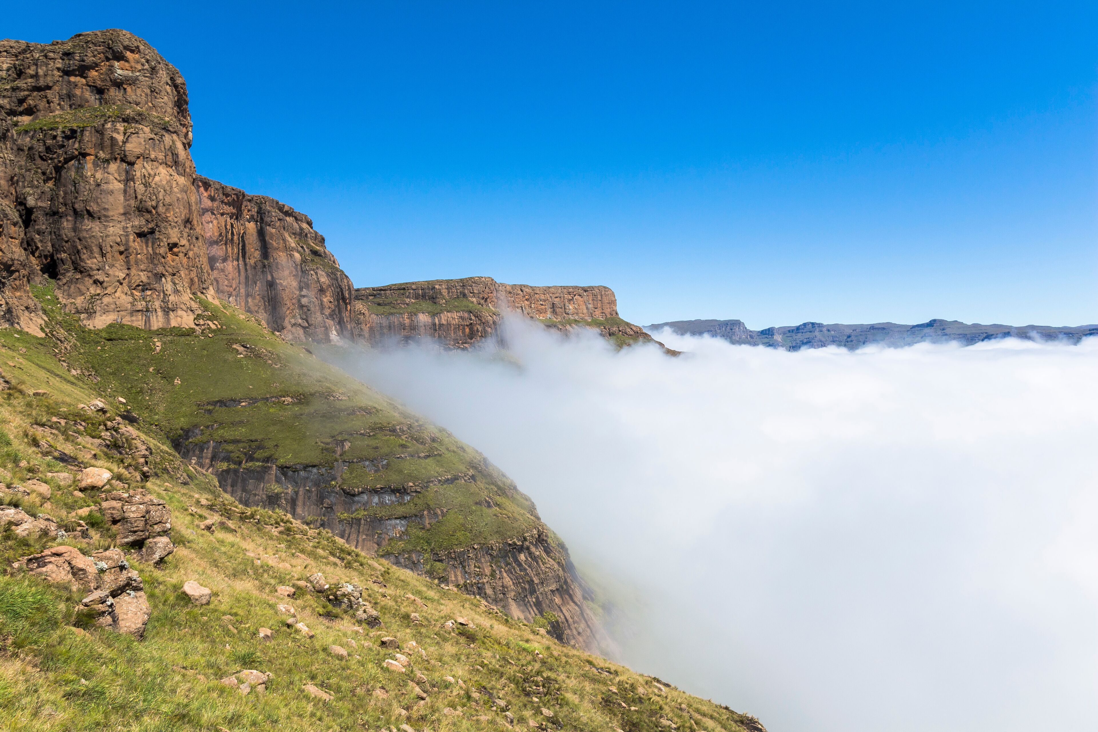 A mountainous landscape with cliffs and a valley shrouded in clouds.