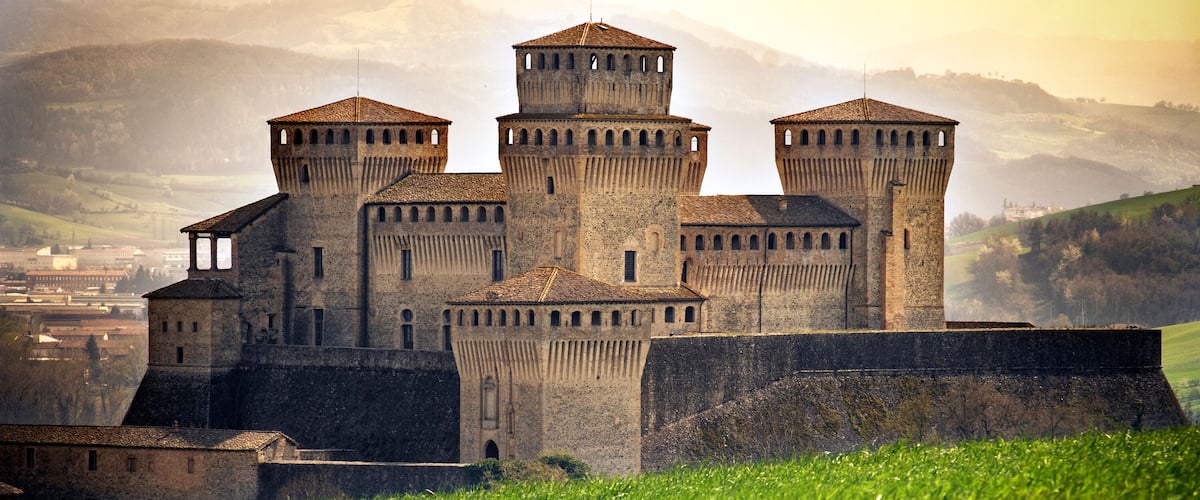 Un château médiéval doté de trois tours et entouré d’un rempart, situé dans un paysage montagneux.