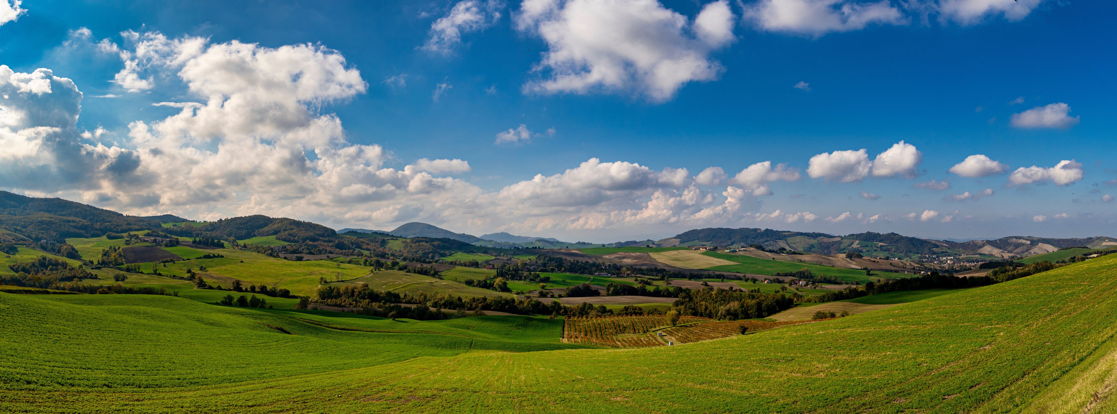 Rolling green hills, a valley, and distant mountains under a partly cloudy sky.