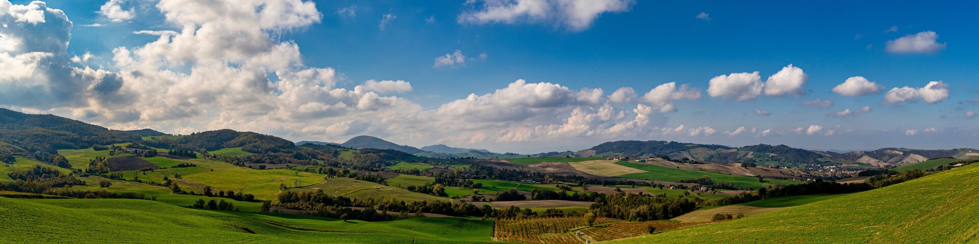 Rolling green hills, a valley, and distant mountains under a partly cloudy sky.