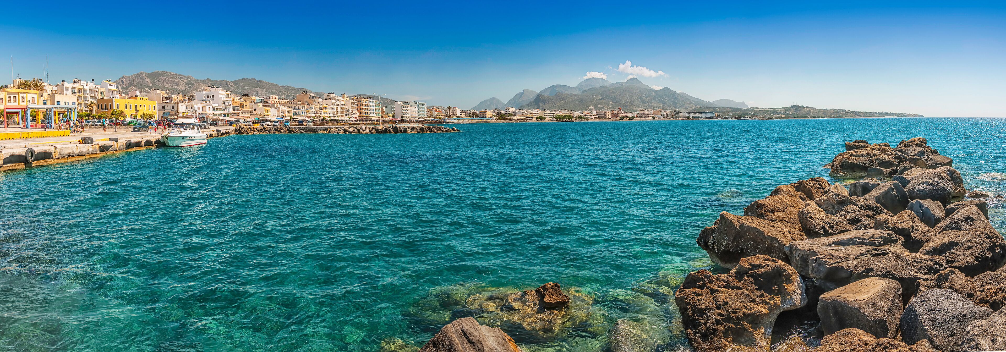 A coastal town with clear blue waters, rocky shore, and colorful buildings.