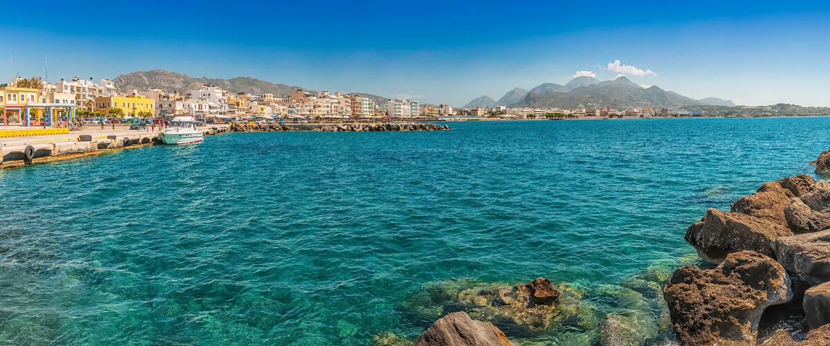 A coastal town with clear blue waters, rocky shore, and colorful buildings.