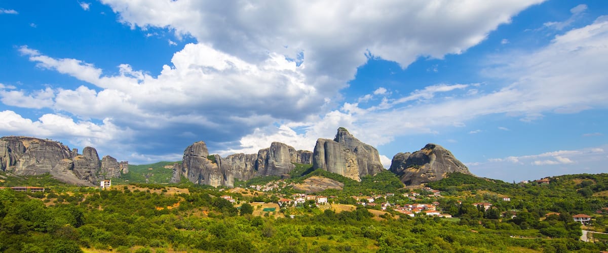 A mountainous landscape with prominent rock formations and a small village nestled among the greenery.
