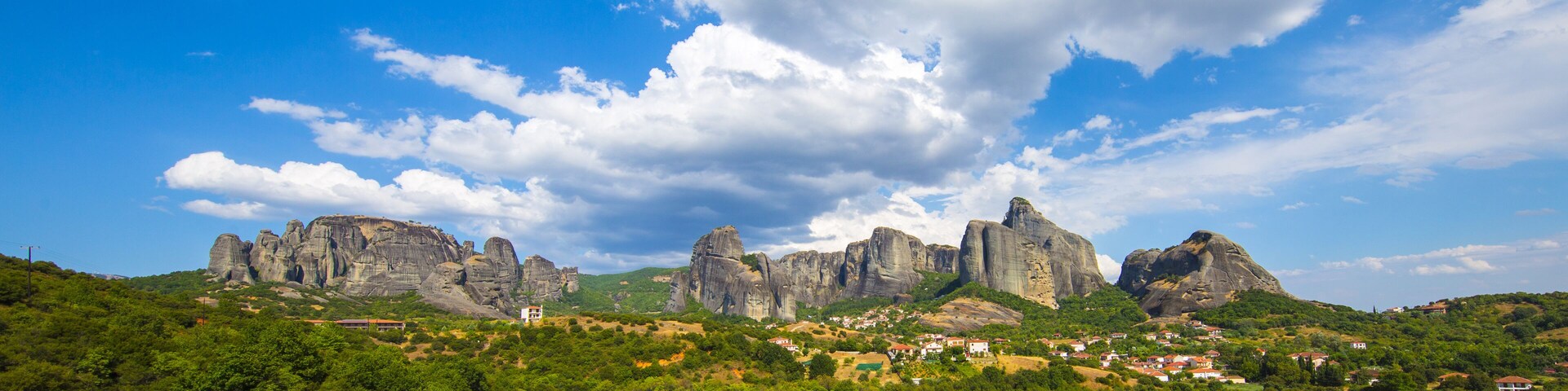 A mountainous landscape with prominent rock formations and a small village nestled among the greenery.