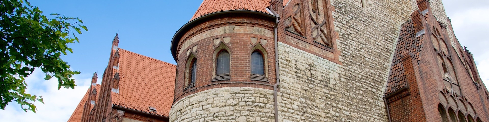 A historic church with a red-tiled roof, stone walls, and a prominent tower with arched windows.