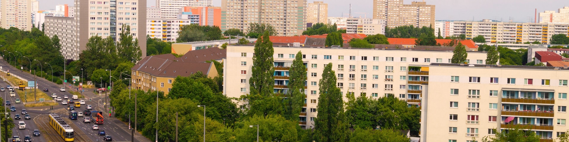 Un paisaje urbano con rascacielos, una calle concurrida con automóviles y un tranvía, y árboles verdes y frondosos.