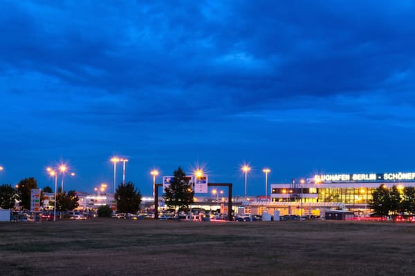 Ein großes Flughafenterminal im Abendlicht mit beleuchteten Schildern und der umliegenden Infrastruktur.