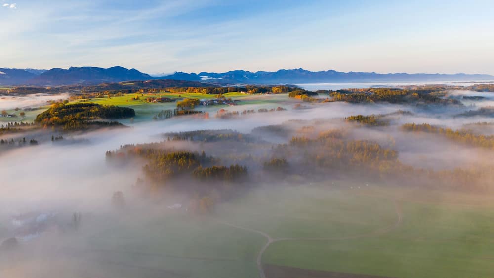 Un paysage brumeux, avec des collines ondoyantes, une rivière et des montagnes lointaines.