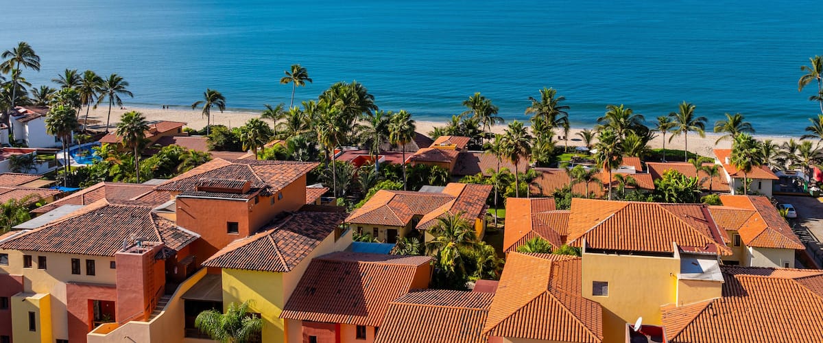 Un pueblo costero con edificios de tejas color terracota, palmeras y una playa.