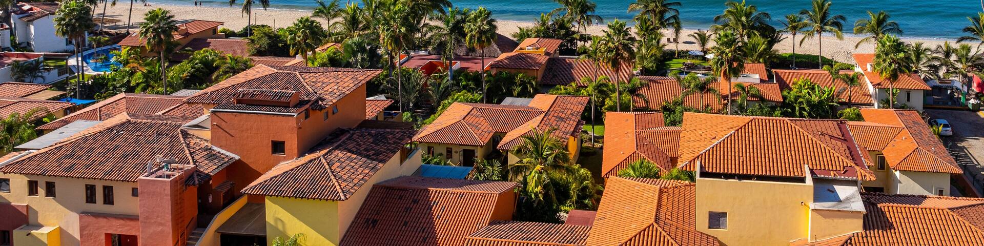 A coastal town with terracotta-roofed buildings, palm trees, and a beach.