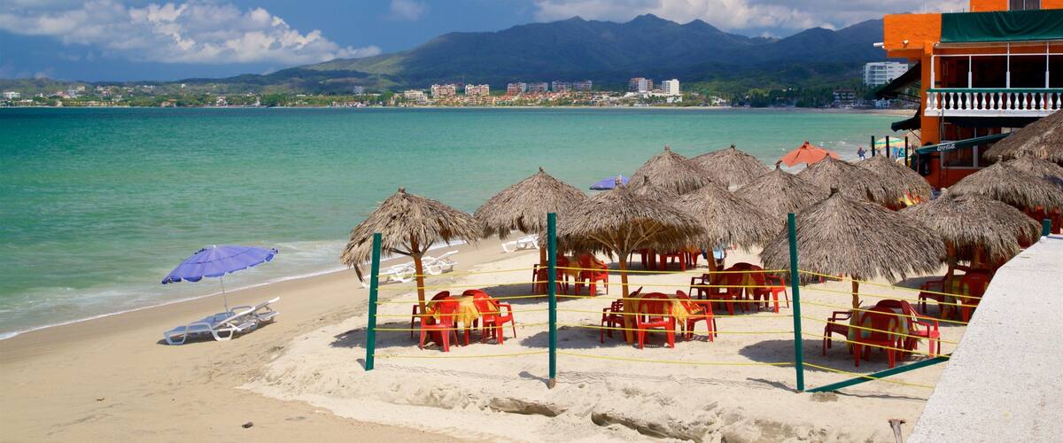 A beach with thatched umbrellas, red chairs, and a clear view of the ocean and mountains in the background.