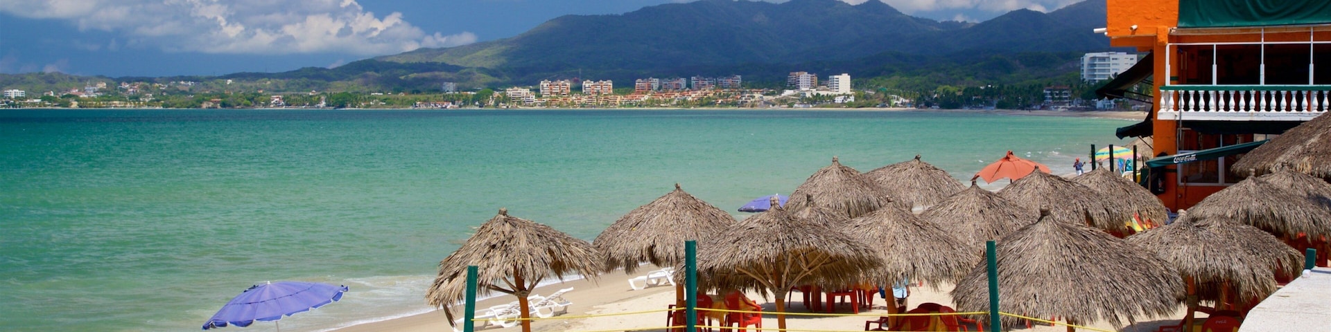 A beach with thatched umbrellas, red chairs, and a clear view of the ocean and mountains in the background.