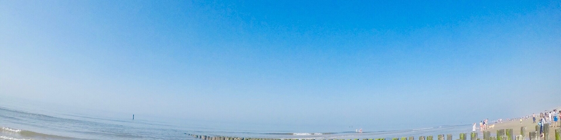 A beach with wooden groynes and people walking along the shore.