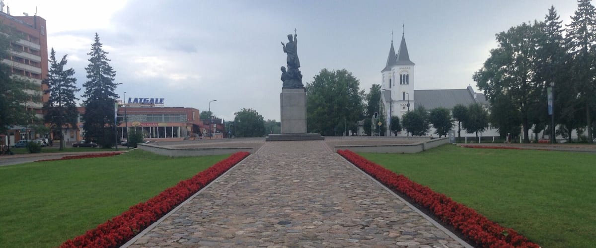 A stone pathway leading to a statue, surrounded by red flowers and trees.