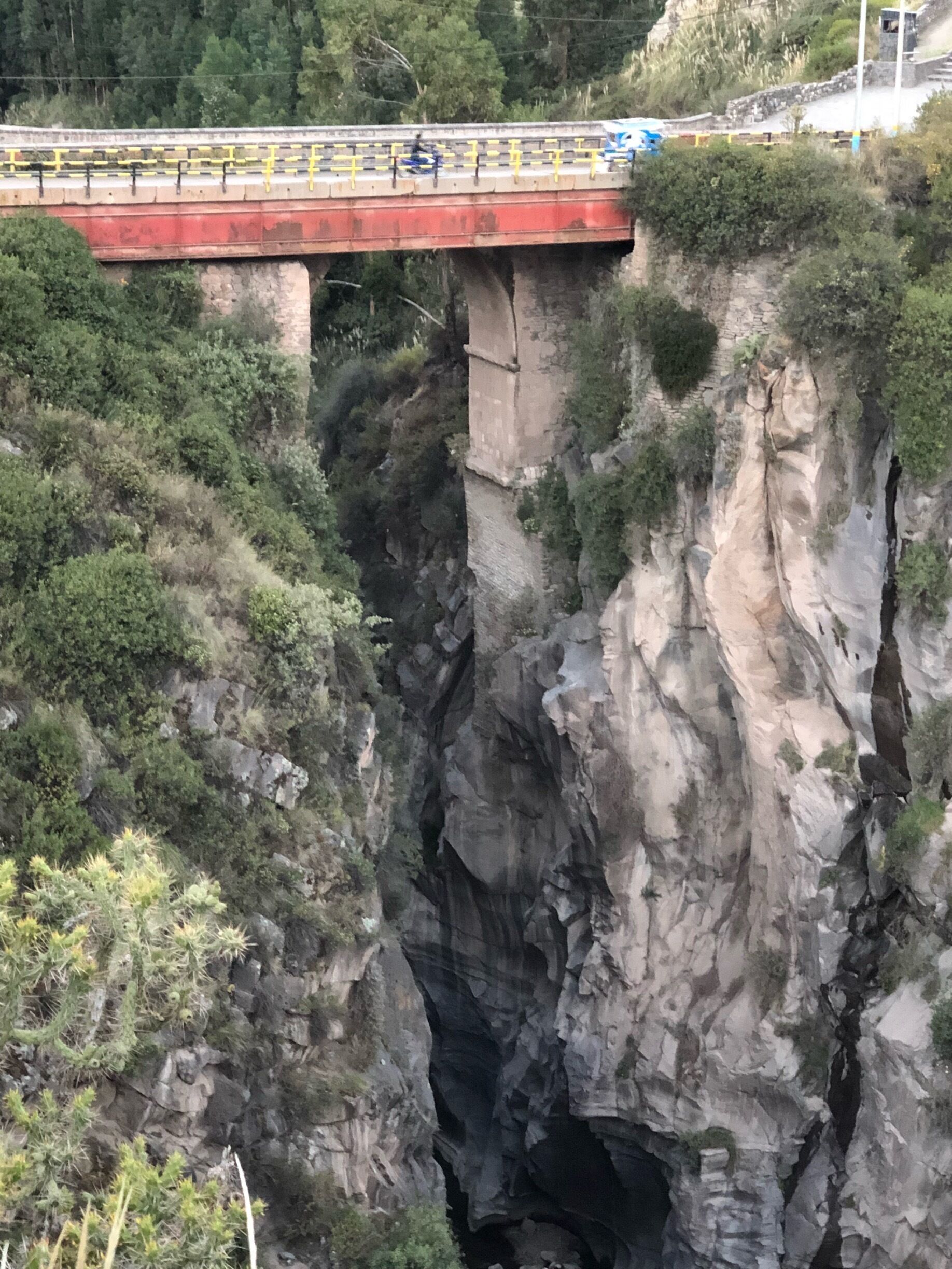 A bridge over a deep canyon with rocky cliffs and sparse vegetation.