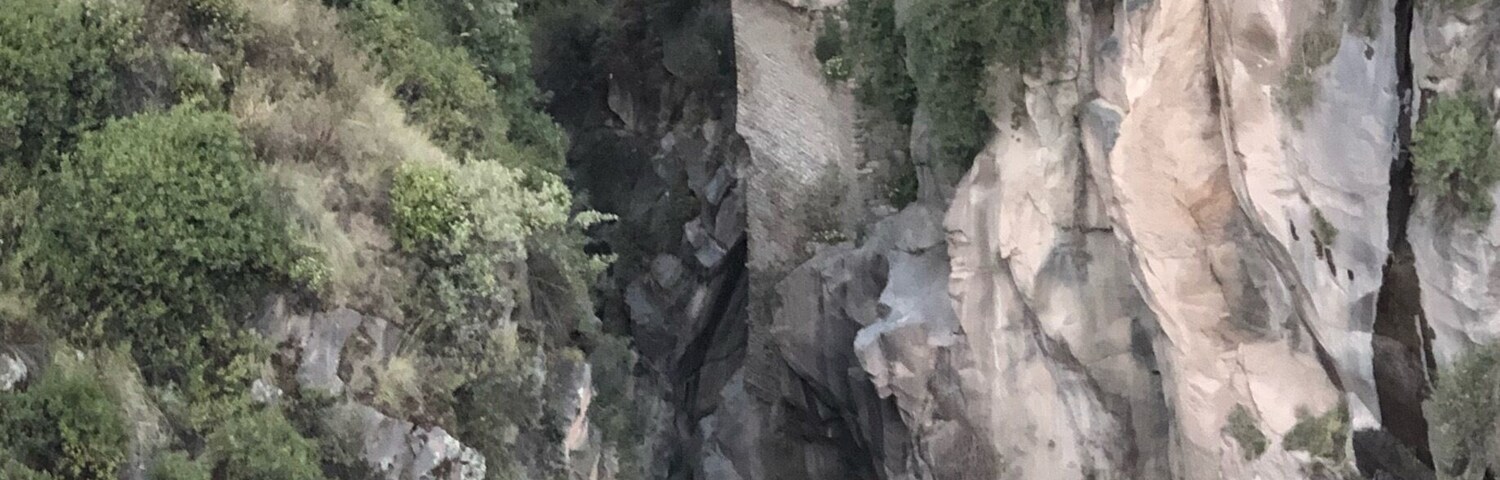 A bridge over a deep canyon with rocky cliffs and sparse vegetation.
