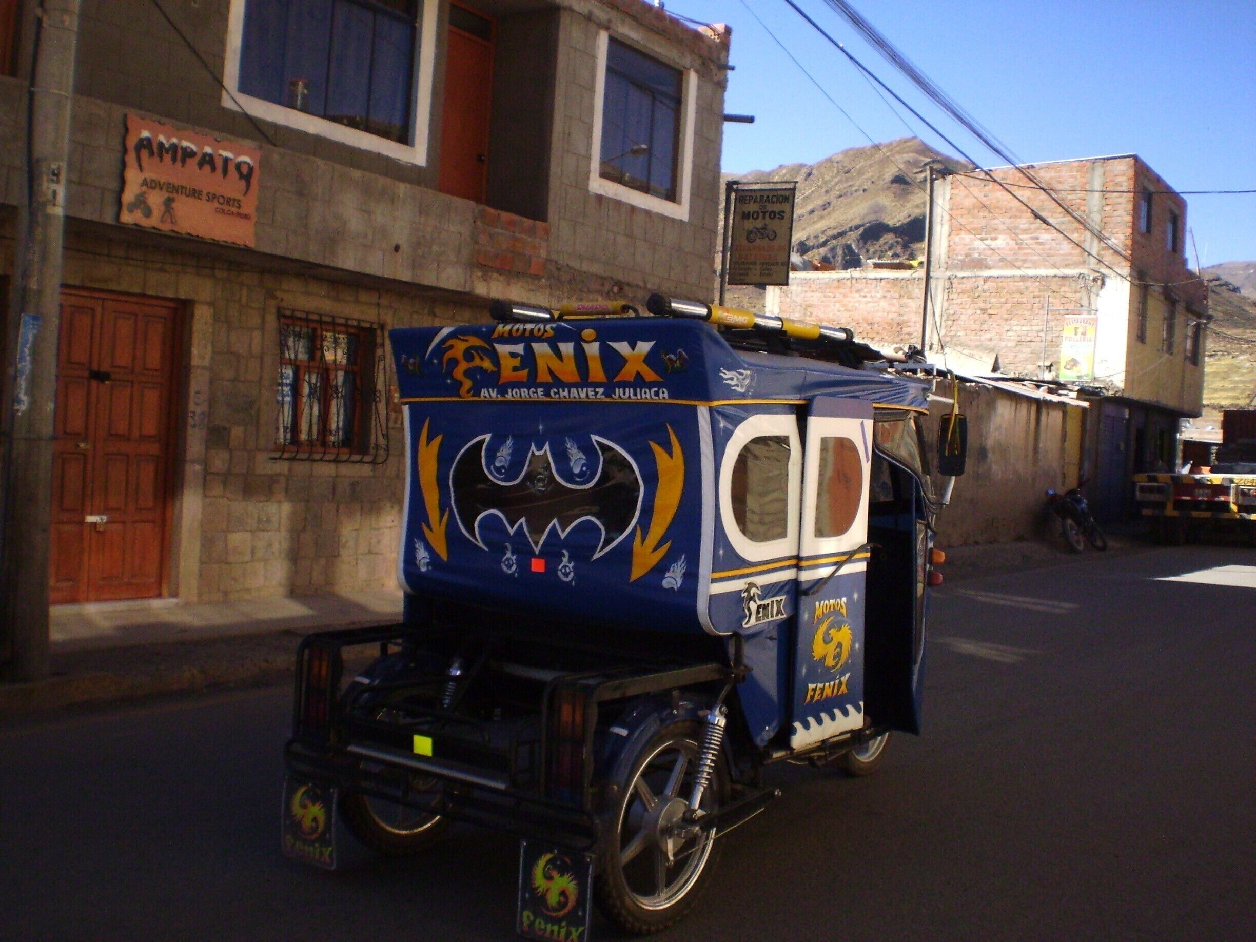 A blue motorcycle with a bat design and 'Penix' branding parked on a street.