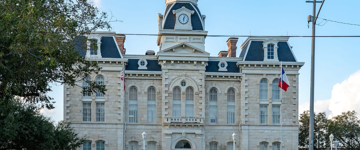 A large stone building with a clock tower, arched windows, and a flag.