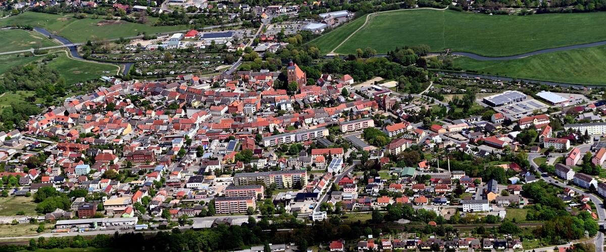 An aerial view of a town with red-roofed buildings, green fields, and a river.