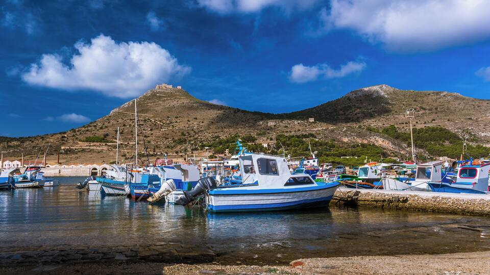 A harbor with boats docked, a mountain in the background, and a clear sky.