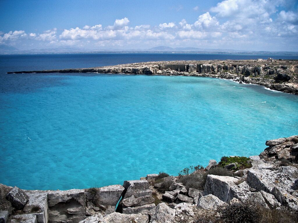 A coastal landscape with clear turquoise waters, rocky formations, and distant buildings.