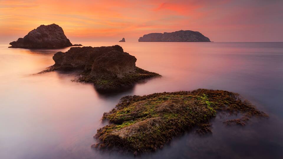 A coastal landscape with rocky formations and calm waters during sunset.