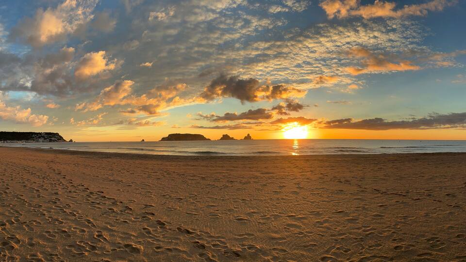 A beach with footprints, a sunset, and distant landforms.