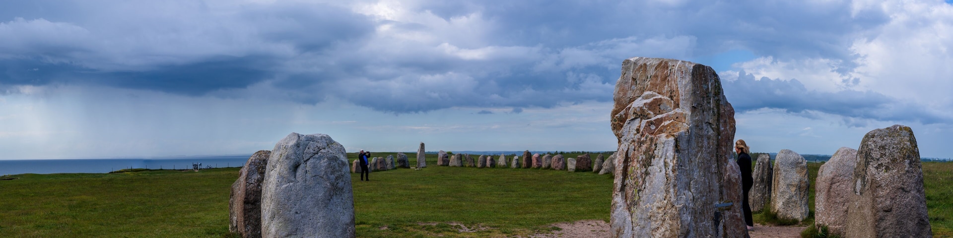 Um círculo de pedra com grandes pedras verticais em um campo gramado sob um céu nublado.