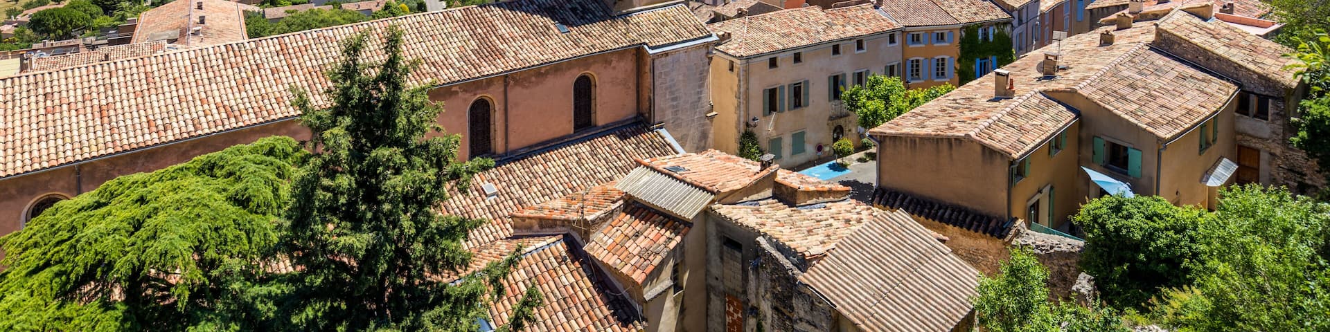 A town with a prominent church tower, terracotta-roofed buildings, and a hilly landscape in the background.