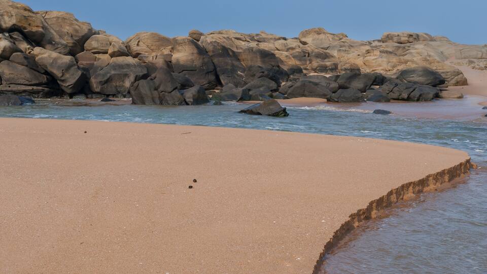 A sandy beach with large rocks and calm water.